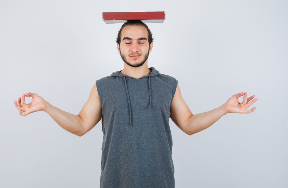Person practicing balance and meditation, red book on head, neutral white backdrop."